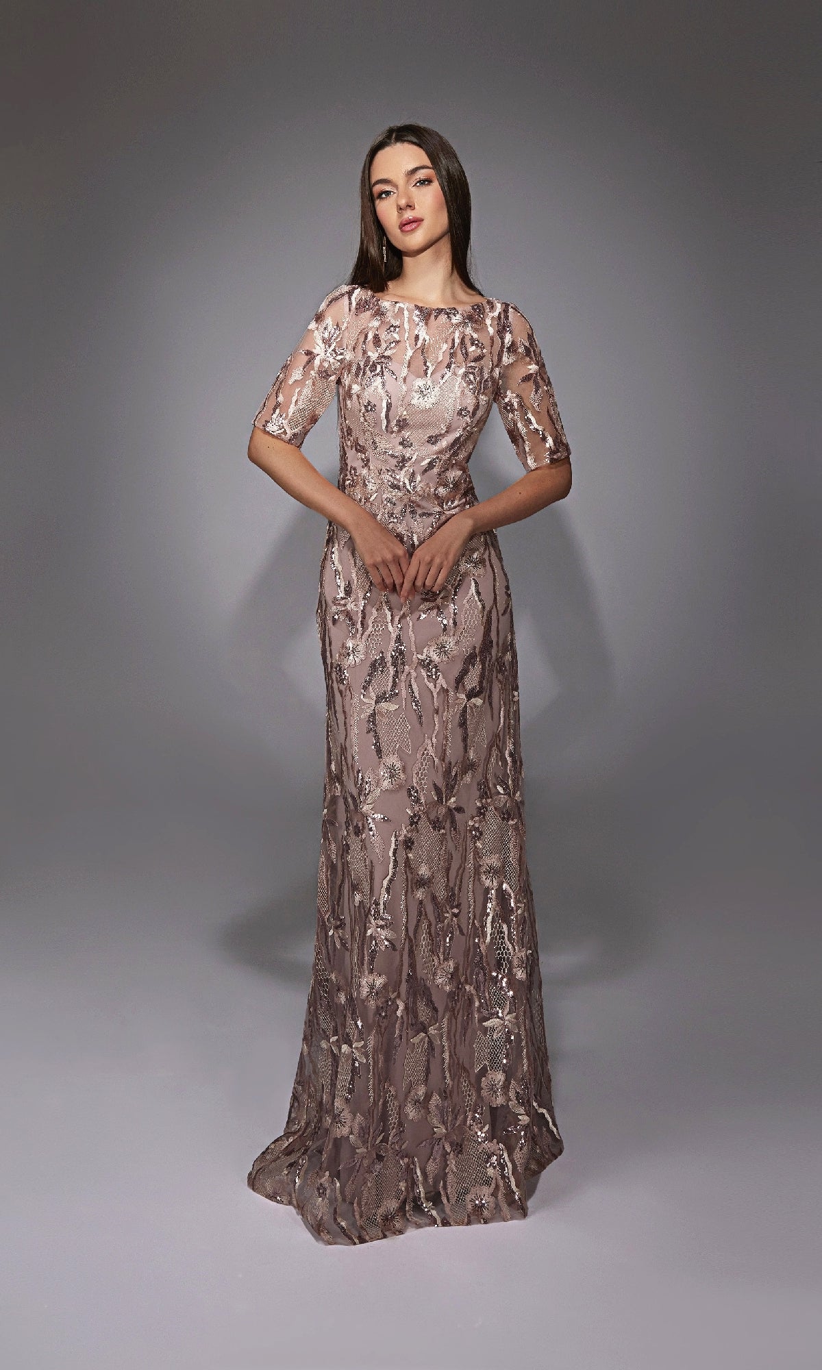 A woman stands wearing the Alyce 27819 long formal dress, a floor-length light mauve gown with sequin and floral embroidery, illusion neckline, sheer short sleeves, and a fitted embellished bodice.